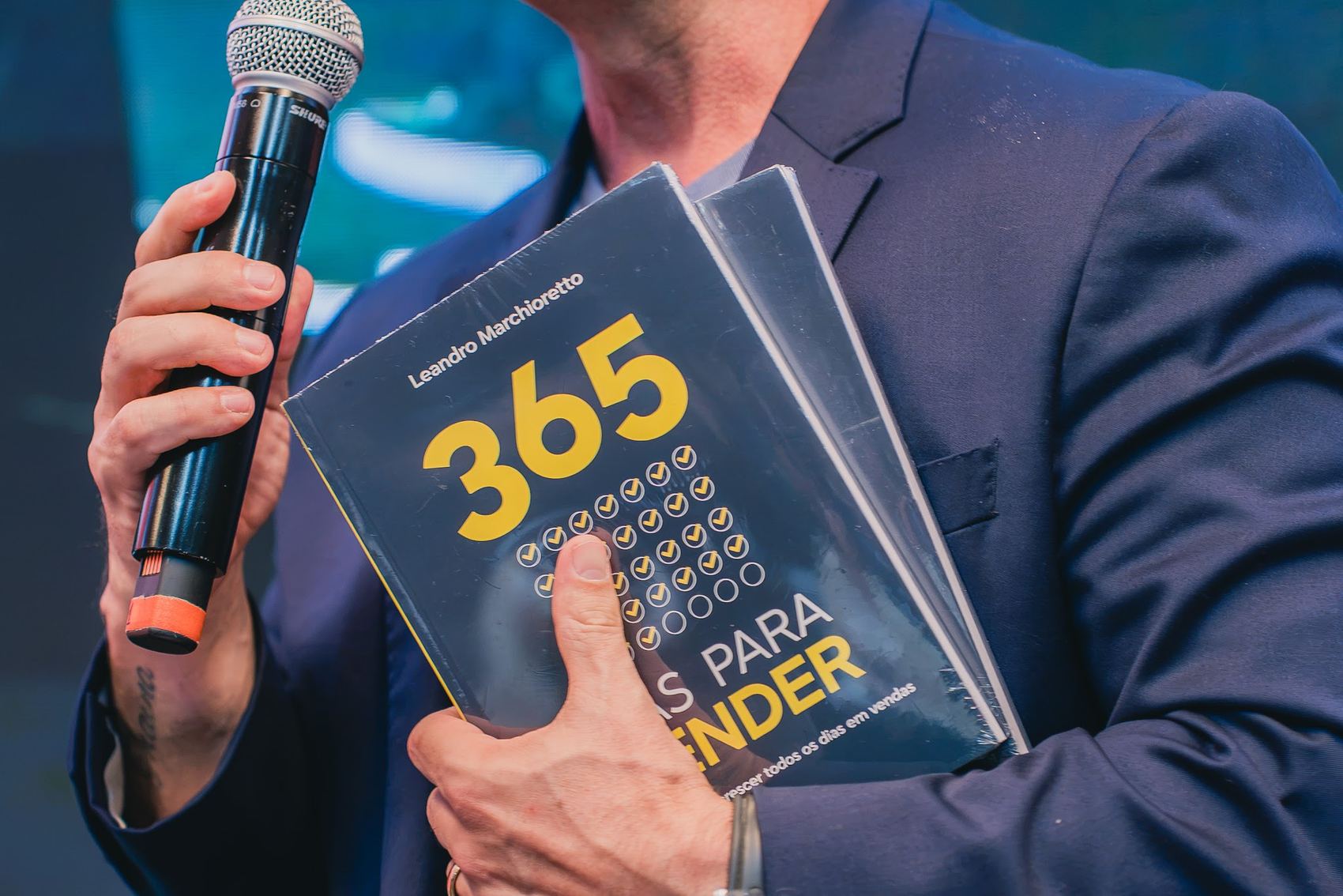Mãos segurando o microfone e o livro 365 dias para vender